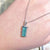 Hand wearing a necklace with a green pendant against an old document background