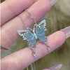 Butterfly-shaped necklace with a light blue stone held between fingers against a blurred background