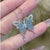 Butterfly-shaped necklace with a light blue stone held between fingers against a blurred background